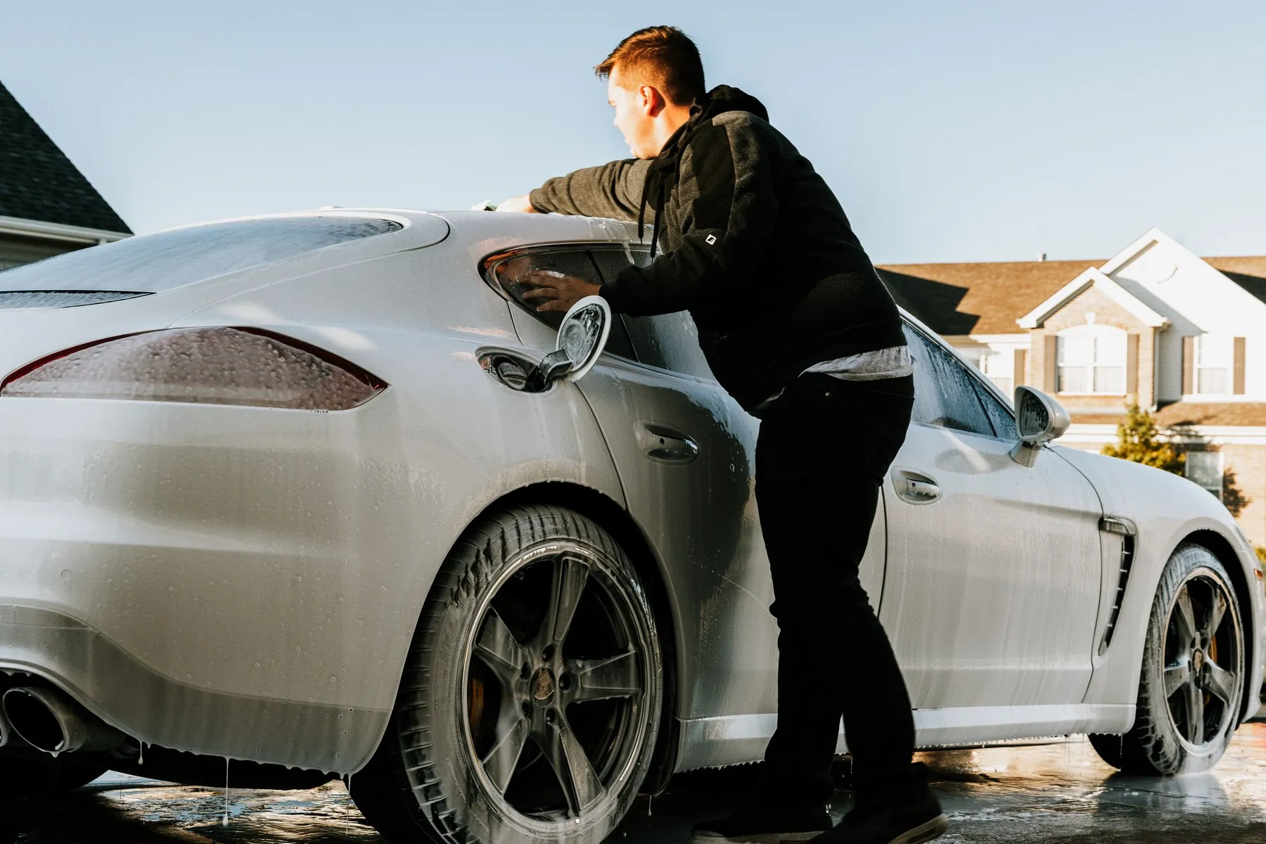 Jacob washing the side of a foam-covered white Porsche Panamera in a driveway