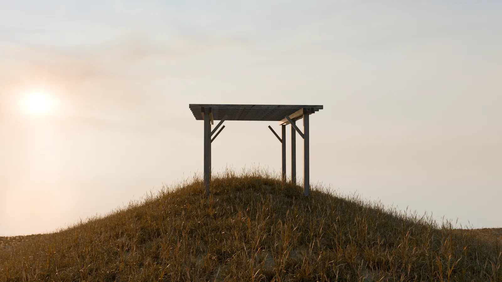 A timber frame standing alone on a grass ridge at golden hour.