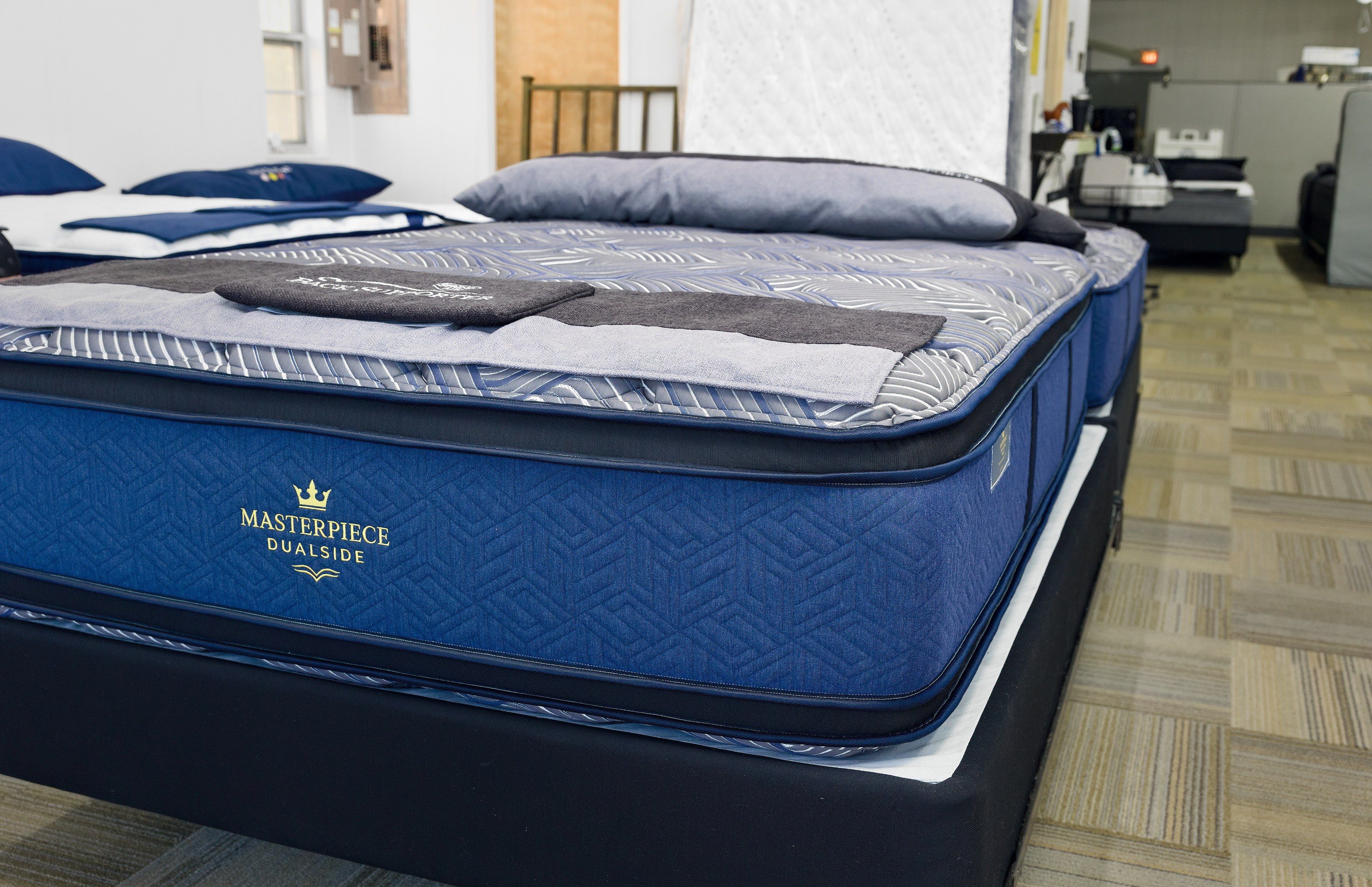 Low view of a Masterpiece DualSide mattress, its quilted navy border and gold crown logo