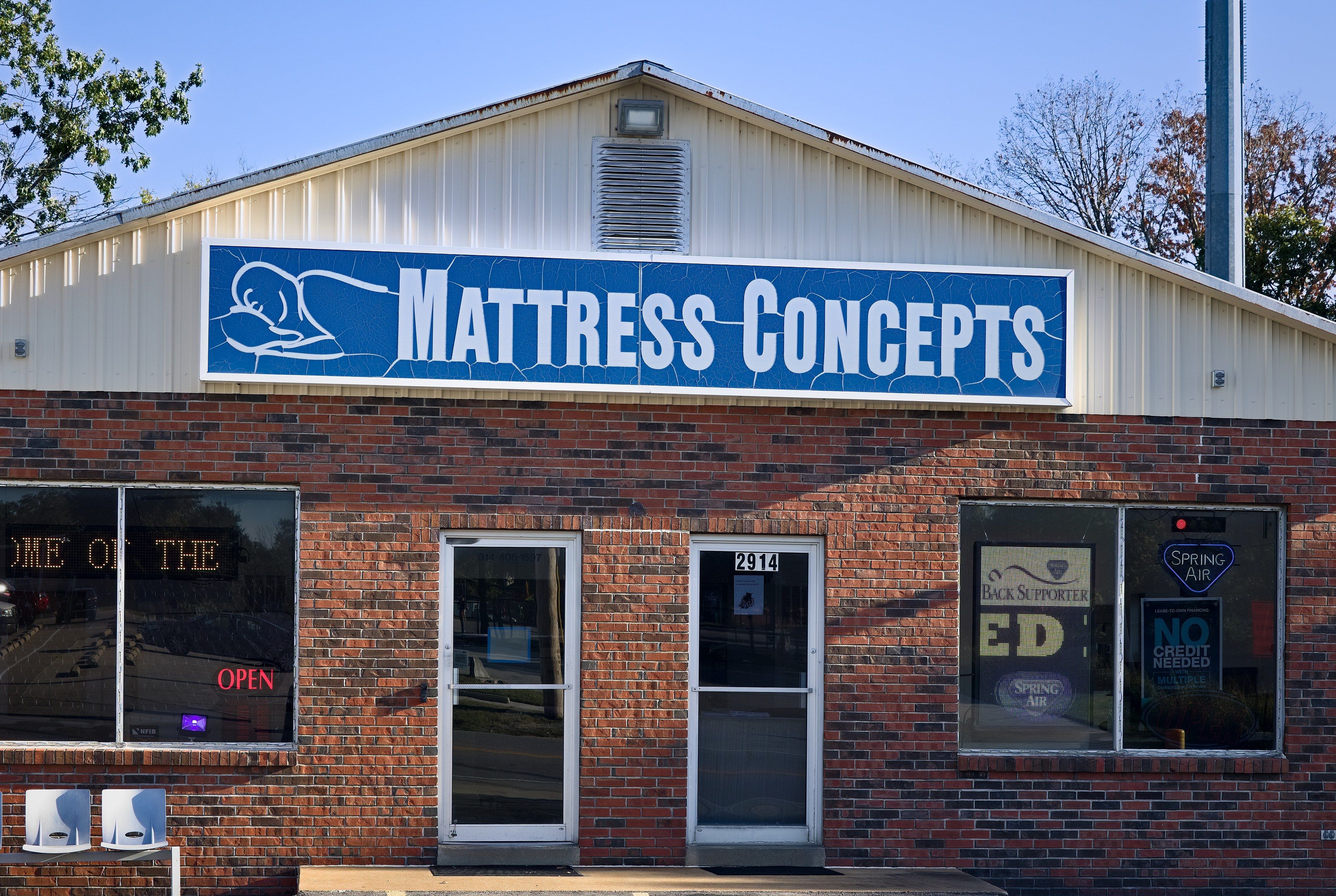 The front of Mattress Concepts in late-day sun: red brick, the blue Mattress Concepts sign and two glass doors