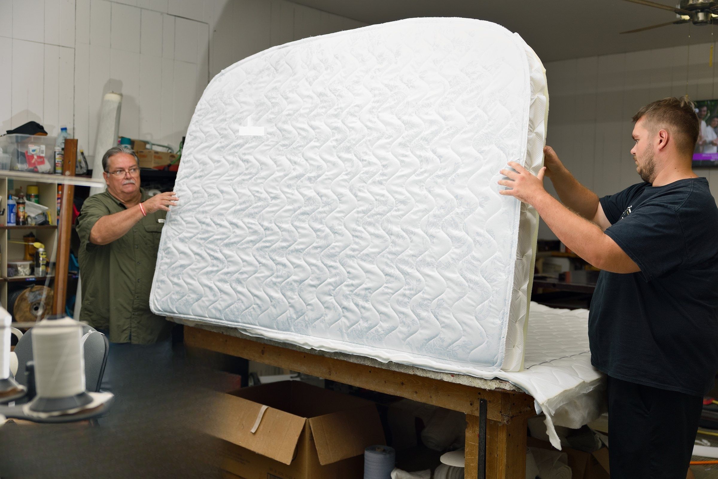 Clinton and a helper standing a finished mattress on its edge in the shop