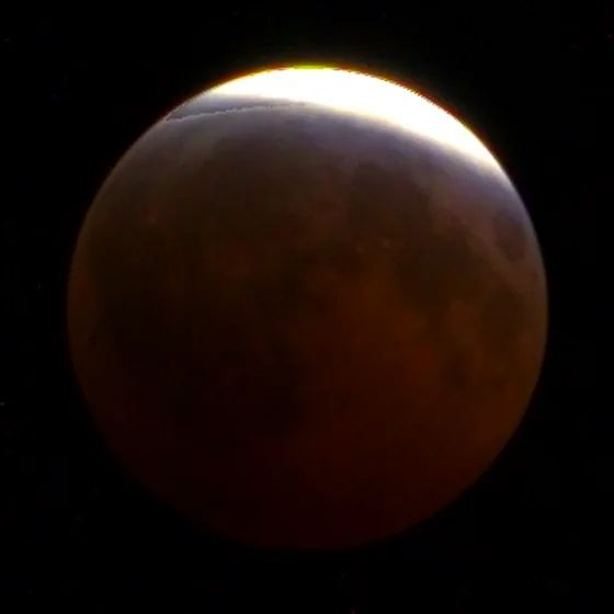 The moon at 22:57, nearly all copper, a thin sunlit edge at the top.