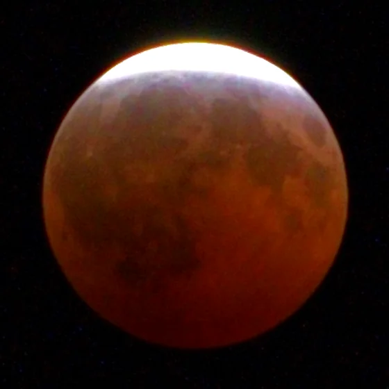 The moon at 23:01, nearly all copper, a thin sunlit edge at the top.