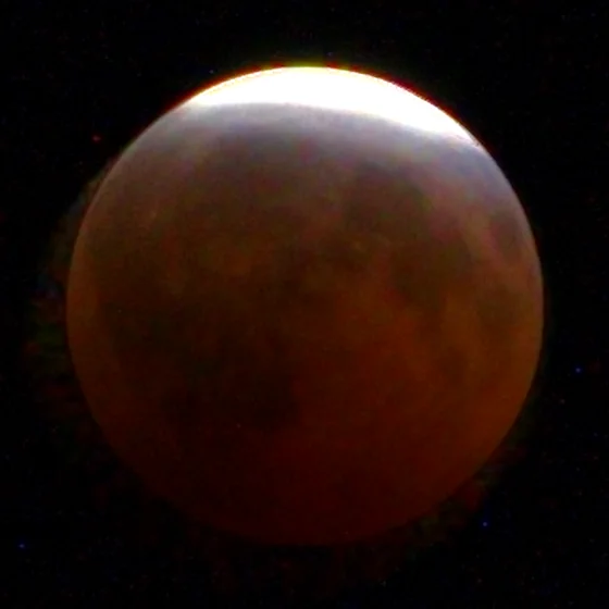 The moon at 23:03, nearly all copper, a thin sunlit edge at the top.