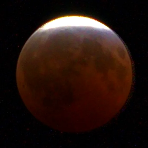 The moon at 23:10, nearly all copper, a thin sunlit edge at the top.