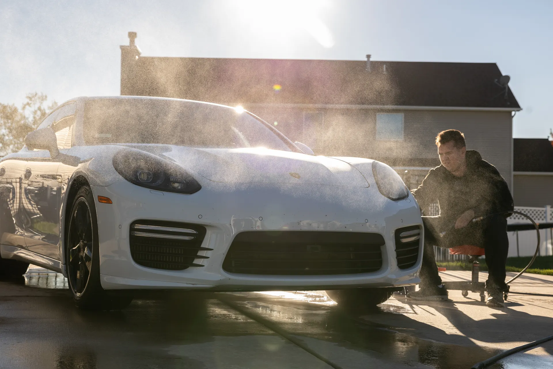 A white Panamera being rinsed into the low sun, spray hanging in the light.