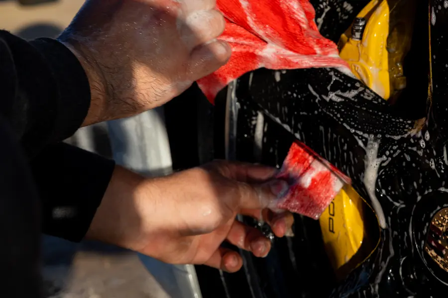 Hands working a red cloth over a yellow brake caliper.