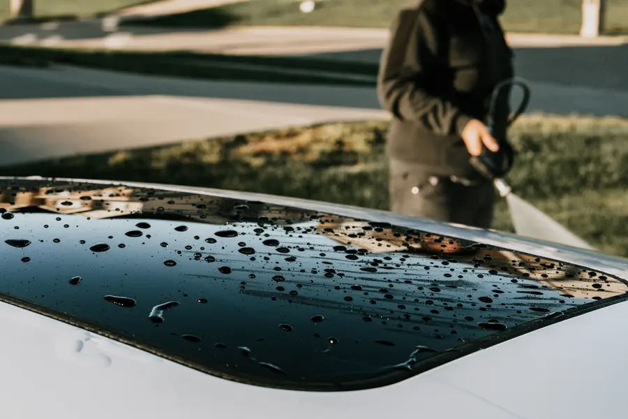Water beading across a dark hood while the detailer rinses behind.