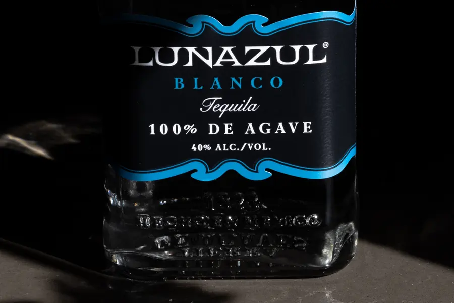 A bottle of Lunazul Blanco tequila lit low against a dark ground.