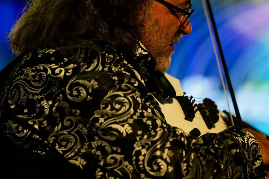 A player in a gold brocade jacket bent over the strings.