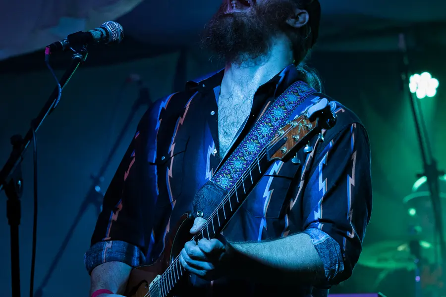 A guitarist under teal light, head down over the neck.