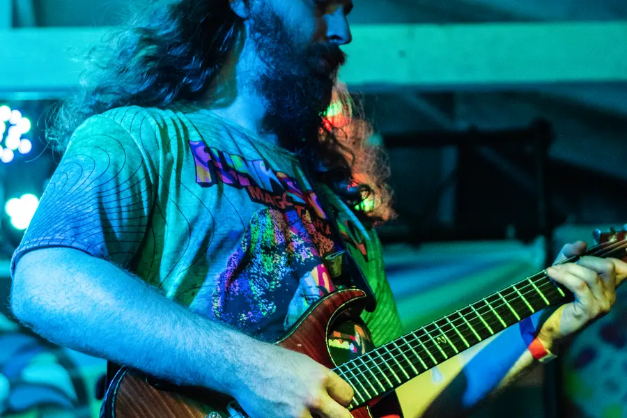 A guitarist lit hard teal and green, mid phrase.