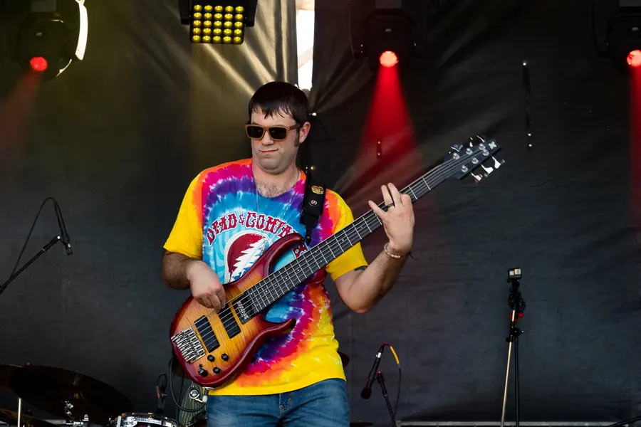 A bassist in a tie dye shirt under red stage light.