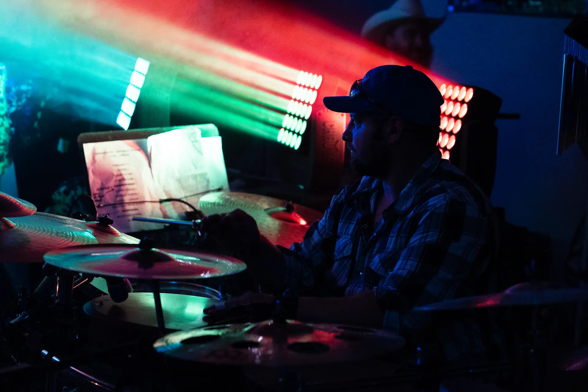 A drummer silhouetted against red and green light bars.