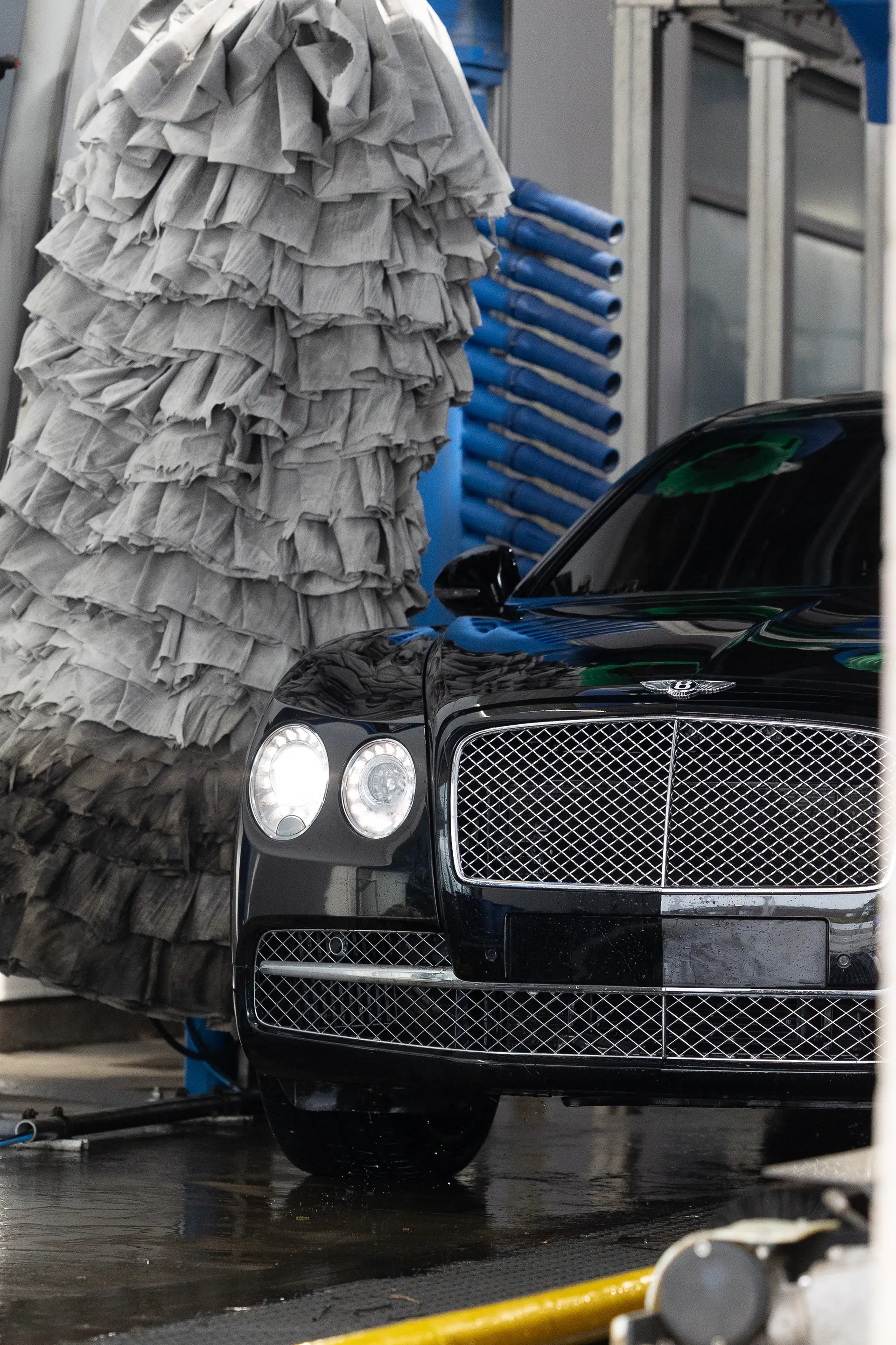 A Bentley grille emerging from grey cloth brushes.