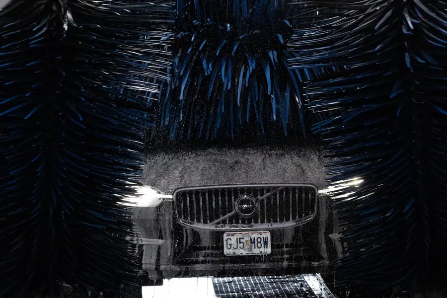 A car nosing through blue tunnel brushes, headlights lit.