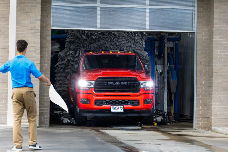 A red pickup coming out of the wash tunnel into daylight.