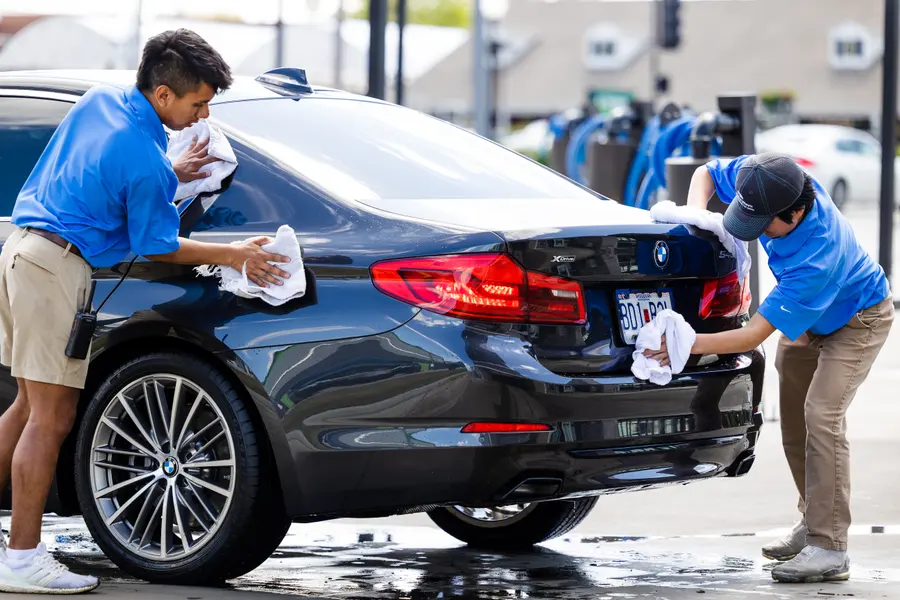 Two staff drying a dark sedan by hand at the vacuum bays.