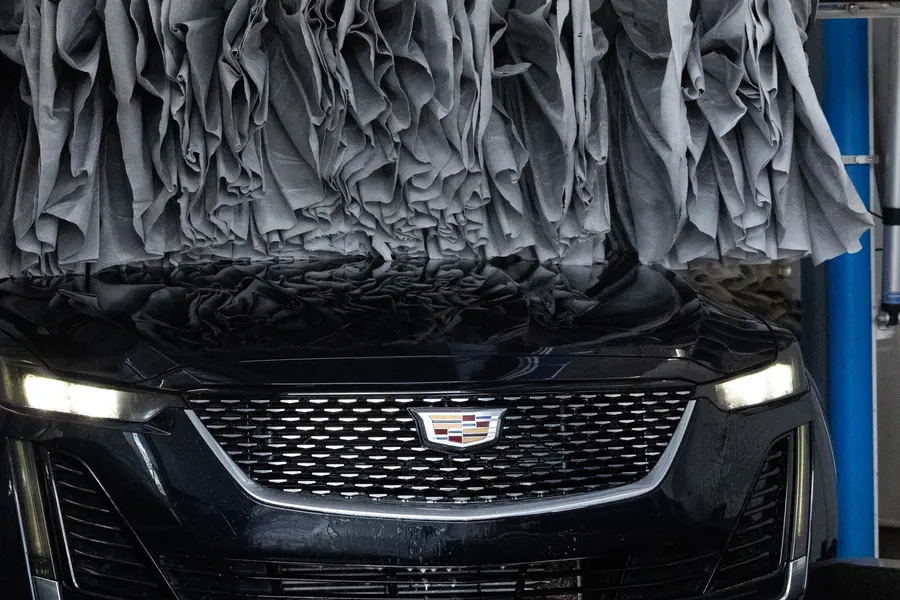 A Cadillac under grey cloth brushes mid wash.