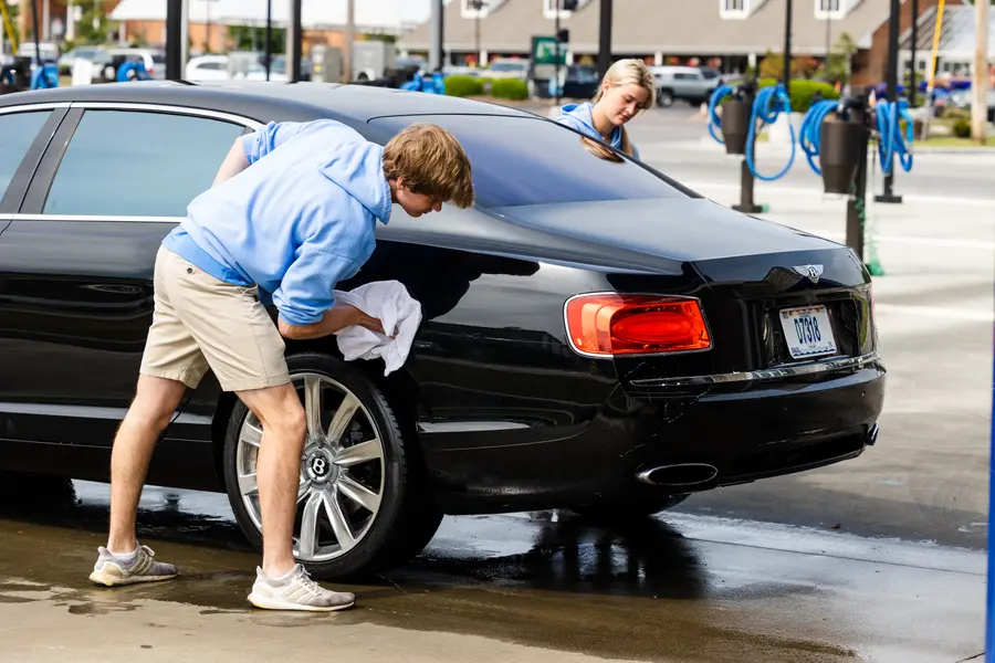 An attendant towelling down the back of a Bentley.